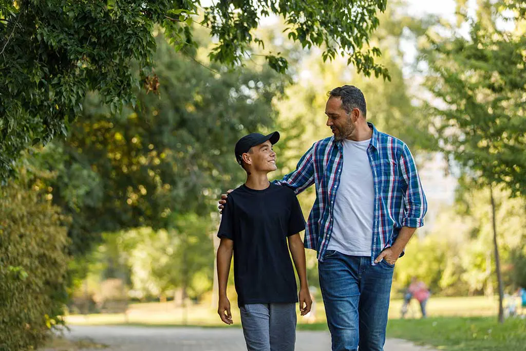 A father and his teen son take a walk in the park and have a nice chat