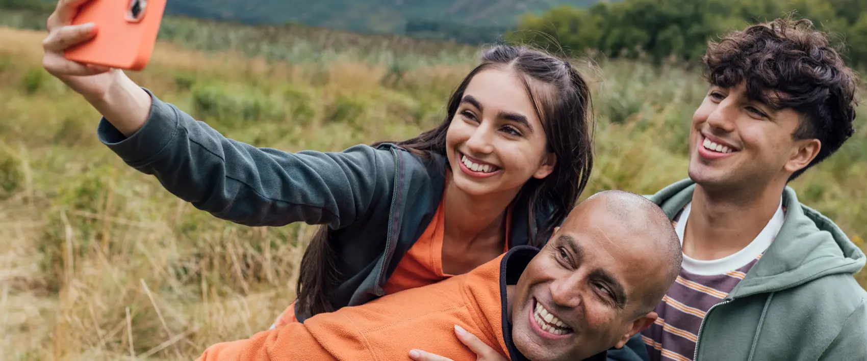 A father and his two teen children pose for a selfie while taking a hike in the wood