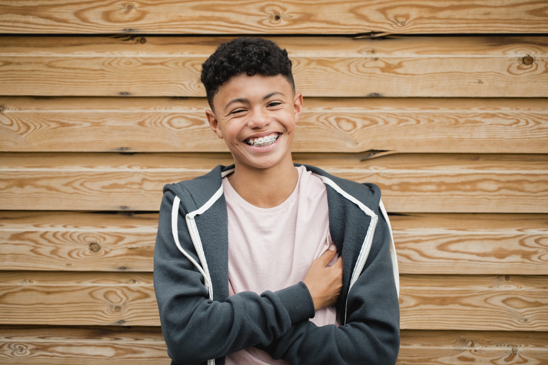A teenage boy with races smiles on a neutral wood backdrop