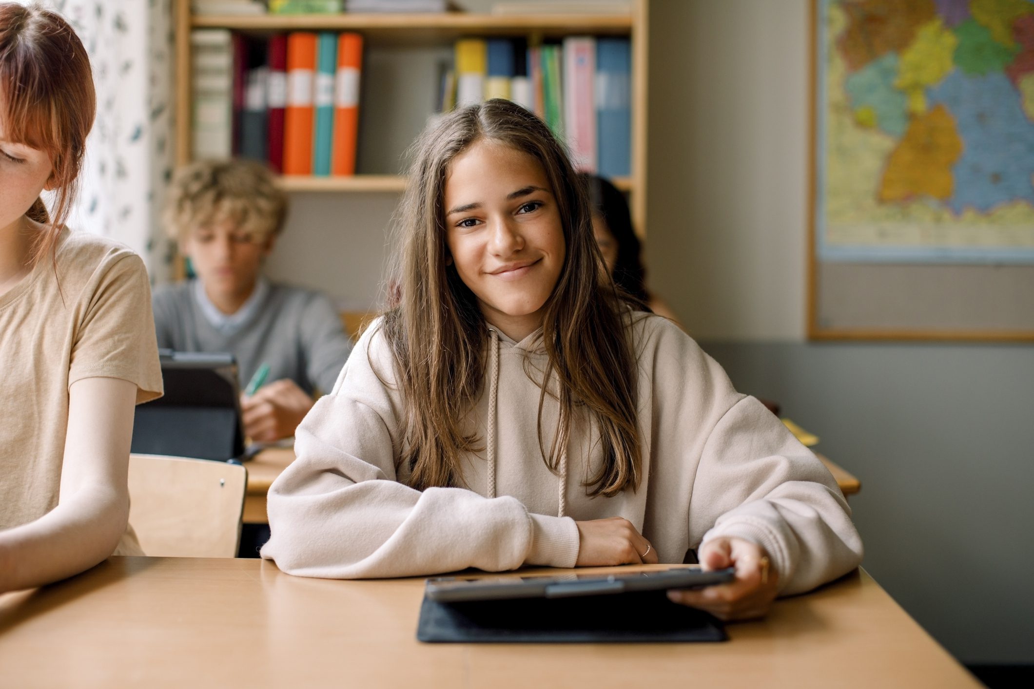 Girl smiling in a classroom while using a tablet to do her school work