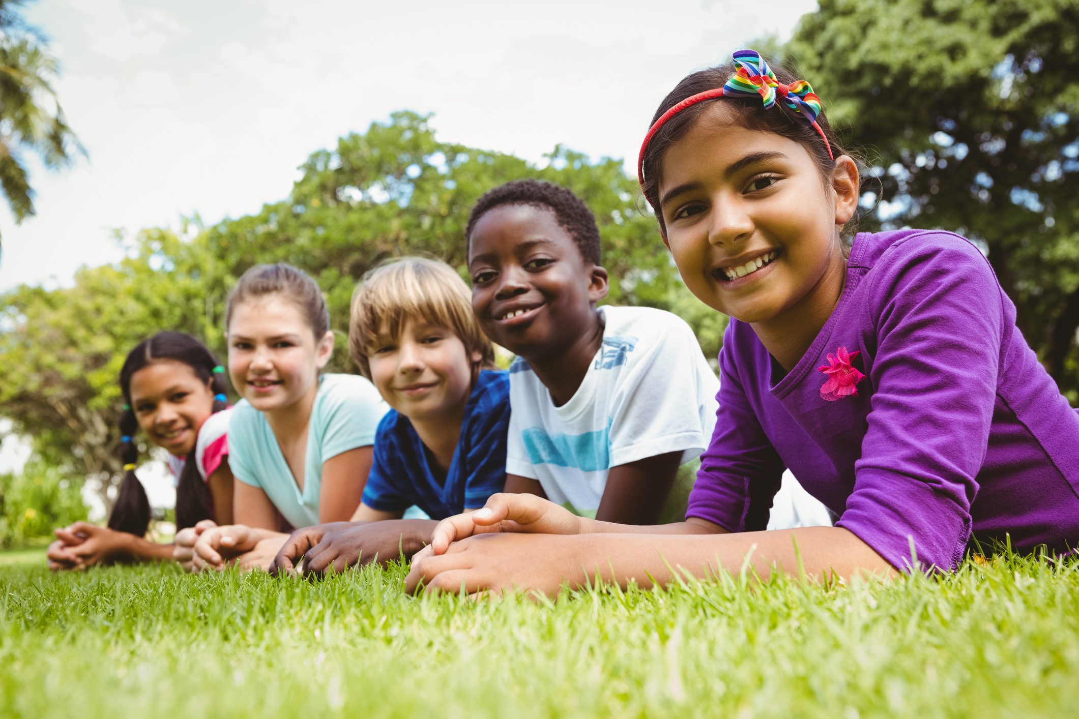 A group of children lay on a grassy field smiling