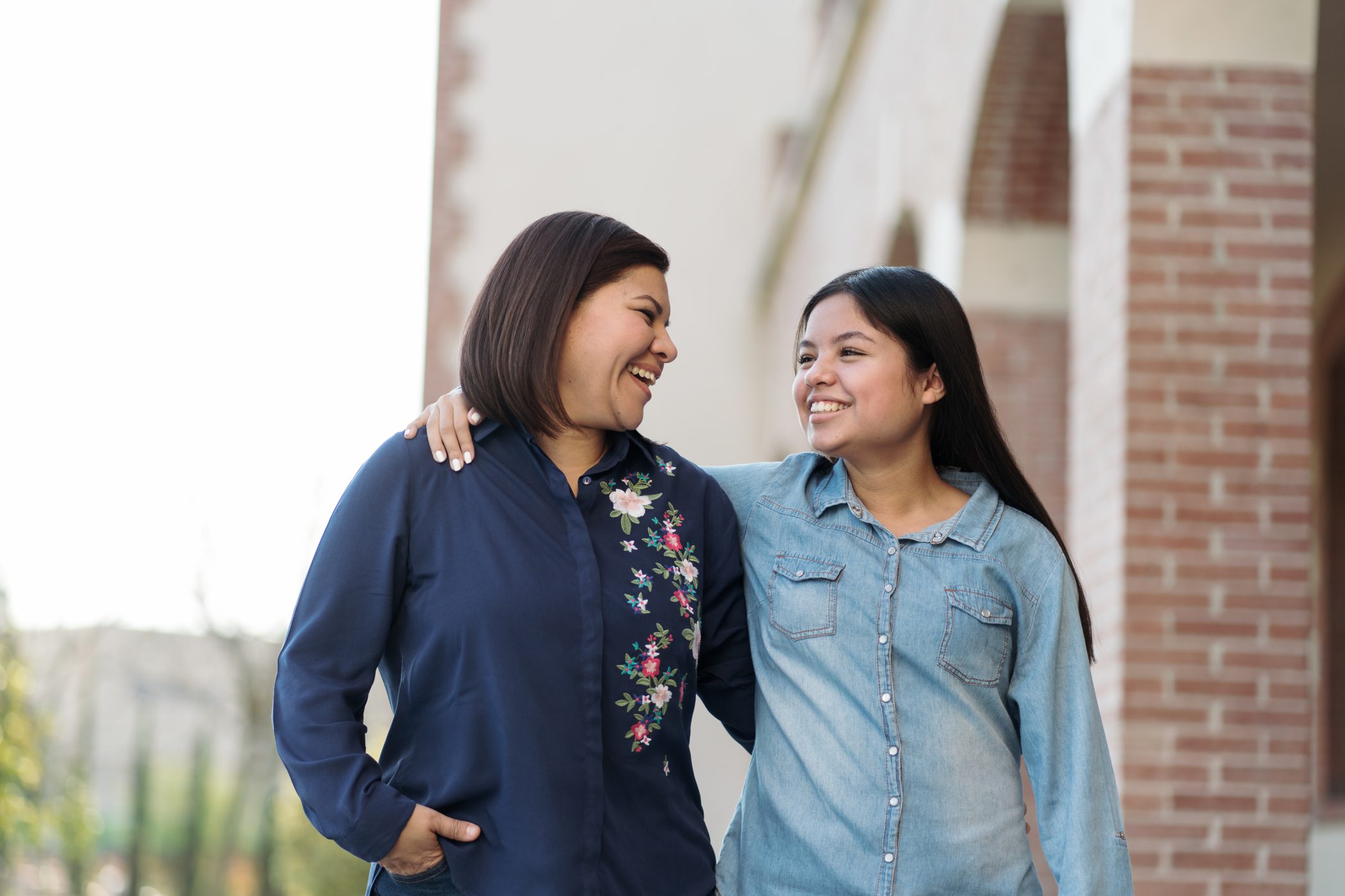 A smiling mother and daughter take a walk while embracing on a sunny day