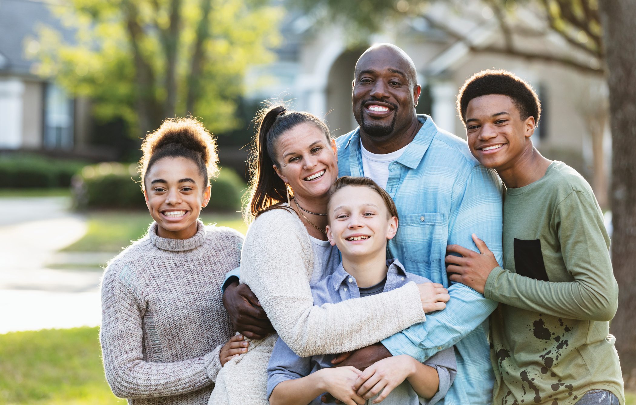 A happy couple with their three children smile and hug while standing in front of their home