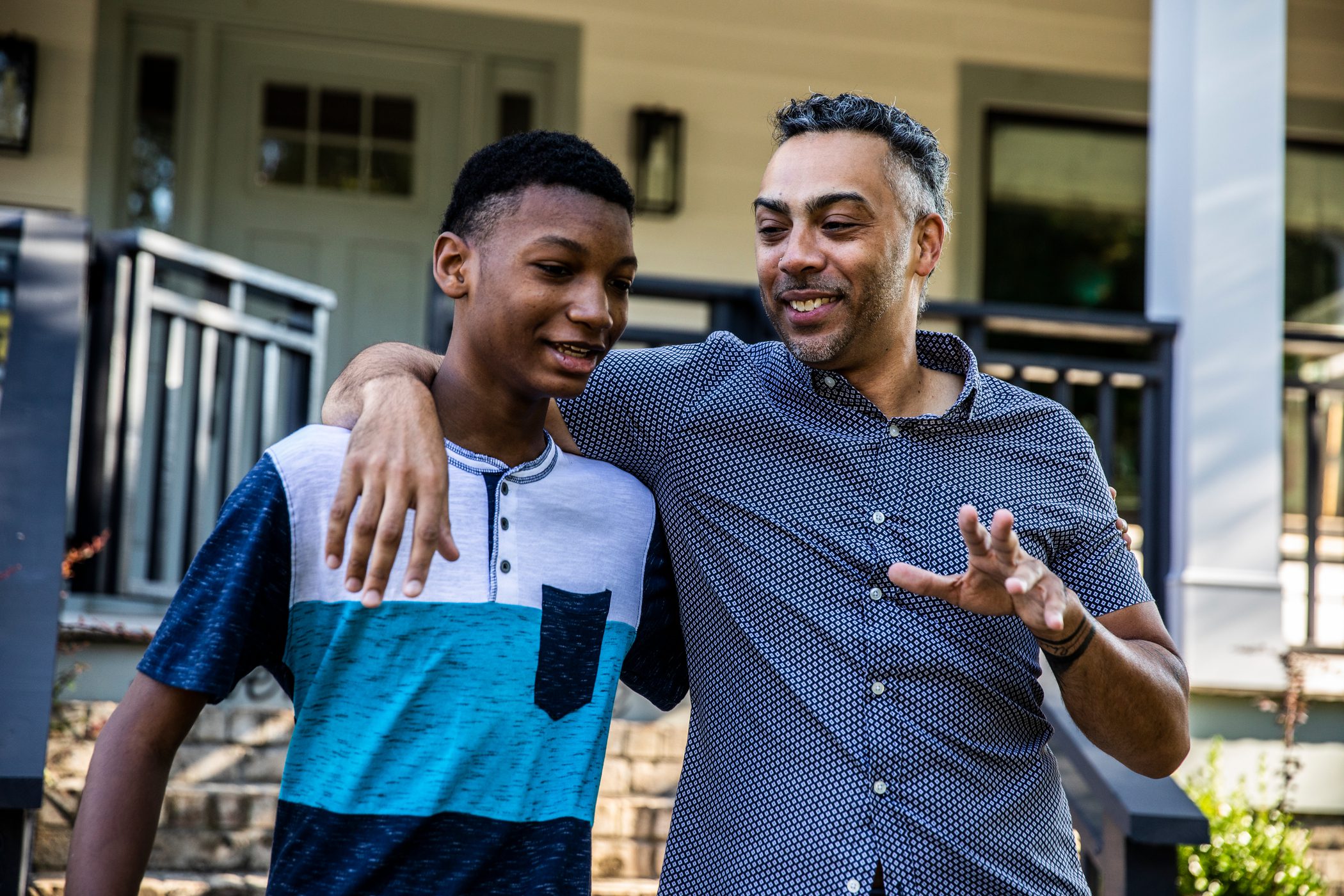 A father wraps her arm around his teen son as they walk in their front yard