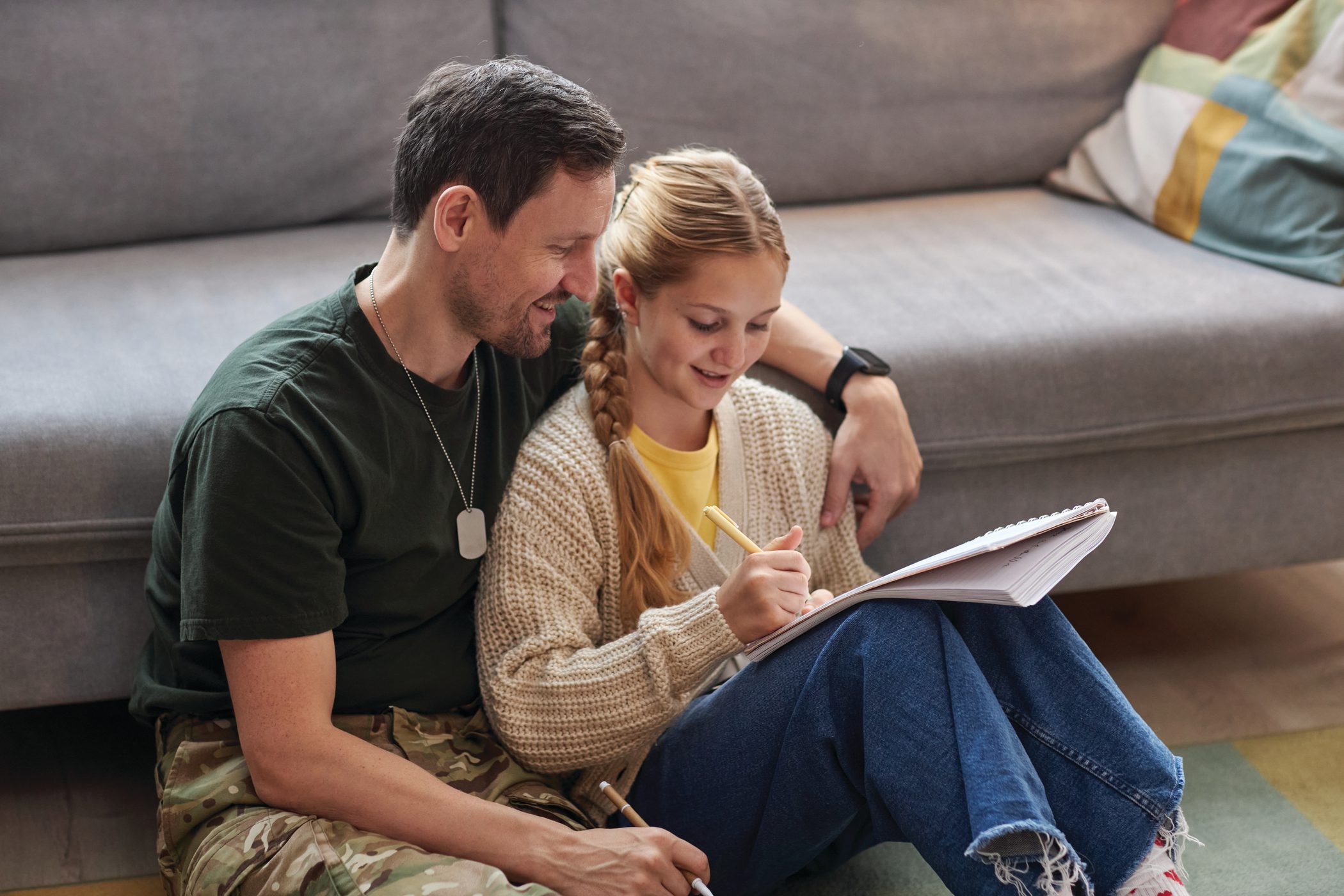 A teenage girls does her homework while being helped by her father, a military member