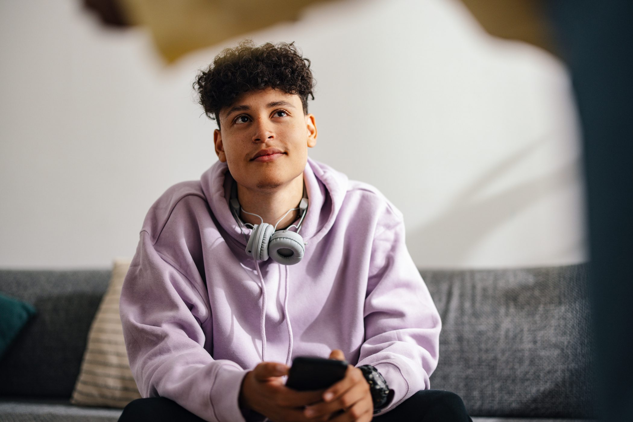 Teen boy wearing a pair of headphones smiles lightly and looks upward