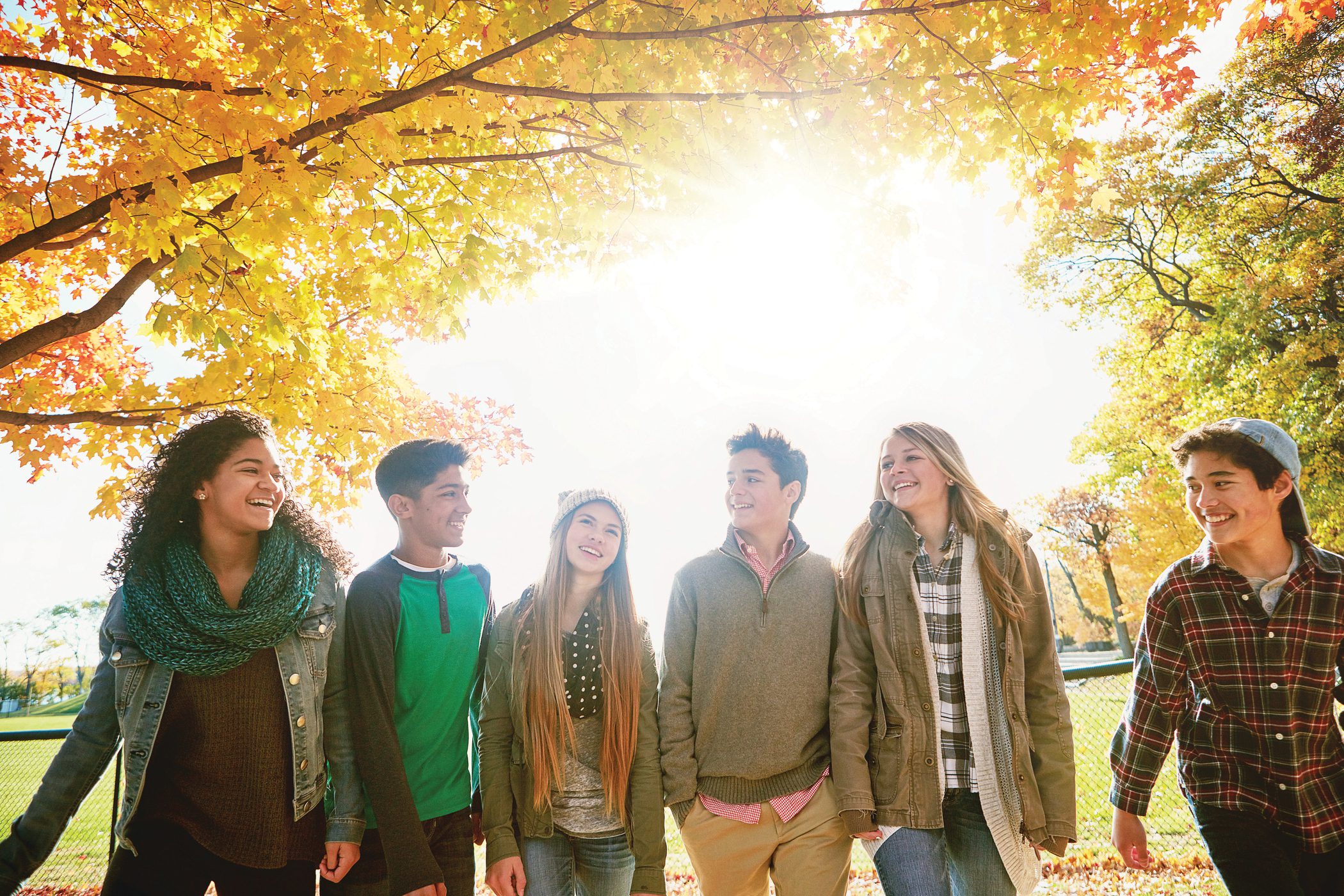 A group of teens take a walk together in the park on a sunny Fall day